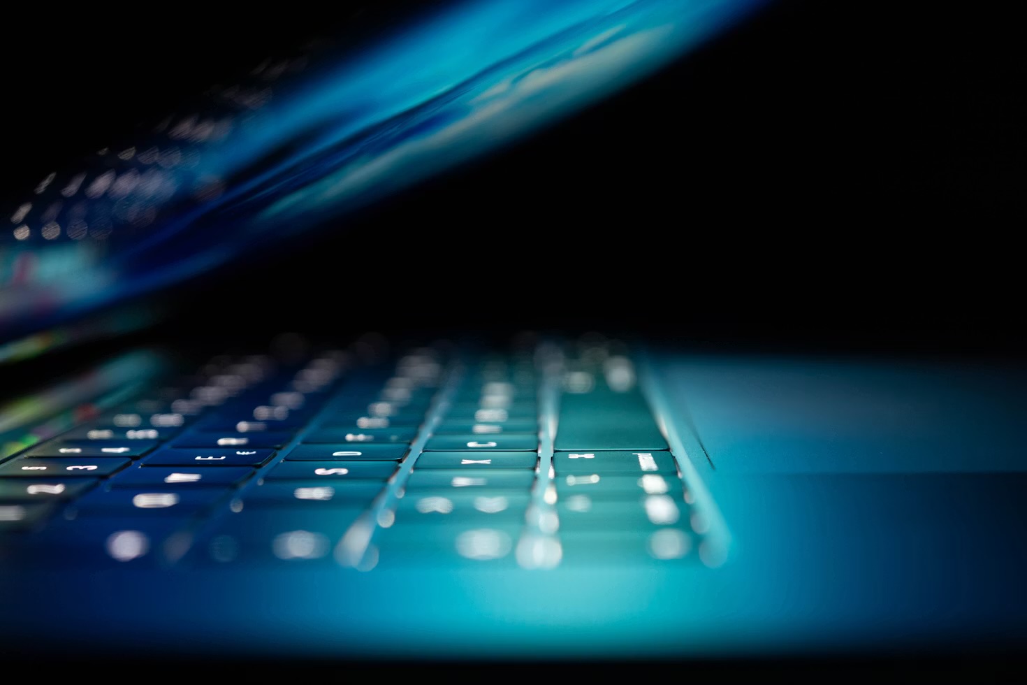 A close-up of hands typing on a laptop keyboard lit in blue