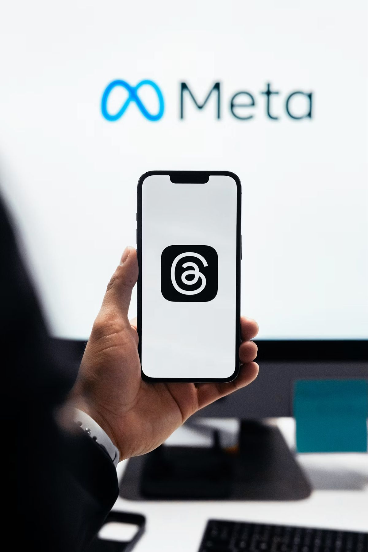 A hand holding a phone with the Meta logo shown on a screen behind it