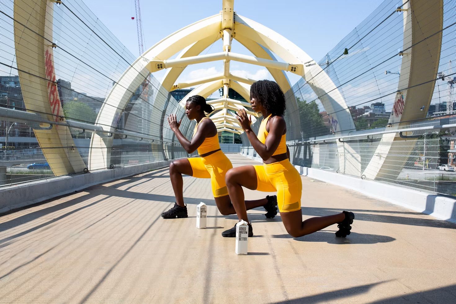 Two women doing lunges outdoors on a bridge